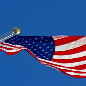 American flag flying on a residential aluminum flagpole against a clear blue Colorado sky