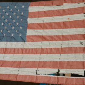 Worn and faded American flag with frayed stripes showing signs it needs retirement and replacement