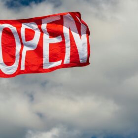 Red custom OPEN advertising flag flying outside a business against a cloudy sky