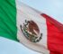The Mexican flag with its eagle emblem waving against a blue sky during Hispanic Heritage Month