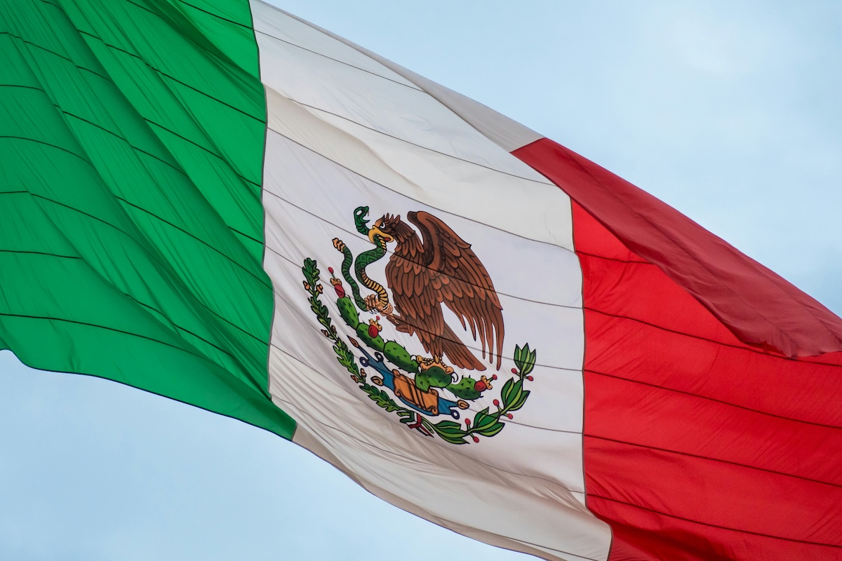 The Mexican flag with its eagle emblem waving against a blue sky during Hispanic Heritage Month