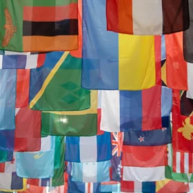 A row of world flags from different nations flying against a blue sky